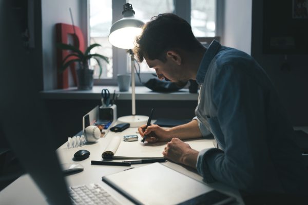 Designer at work in office. Man drawing in note pad